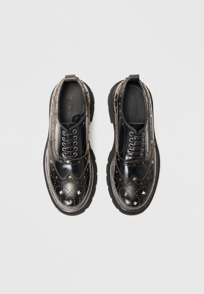 Pantofi din piele lacătă neagră cu detalii brogue, vârf ascuțit și studs argintii. Talpă groasă din cauciuc negru cu �șireturi și bucle de tragere.