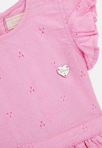 Pink cotton dress featuring floral embroidery, ruffled sleeves, and a heart-shaped silver "Guess" tag.