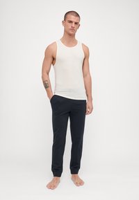 Lys beige tank topp kombinert med mørk marine joggebukser. Bukser med ribbede mansjetter og lommer. Antrekket er enkelt og uformelt.