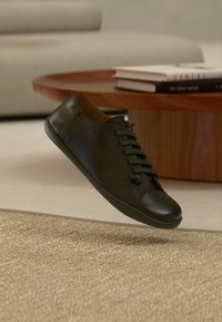 Sneaker in pelle nera con punta arrotondata, lacci piatti e cuciture minime. Texture morbida e suola in gomma a profilo basso.