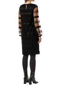 Schwarzes Kleid mit durchsichtigen, gestreiften langen Ärmeln und einem Ausschnitt im Rücken. Der Rock ist glatt mit subtiler Textur und reicht bis zum Knie.