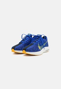 Blaue Sportschuhe aus strukturiertem Strickmaterial, mit gelben Akzenten und schwarzen Details. Ausstattung mit einer weißen Zwischensohle und flexiblem Sohlendesign.