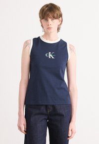 Námornícky bezrúškový top s okrúhlym bielym výstrihom, s zeleno-bielym logom "CK" v strede. Nosené s tmavomodrými džínami.