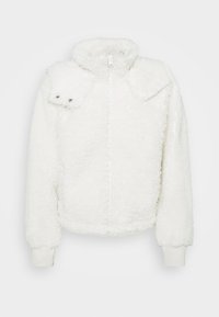 Bílá umělá kožešinová bunda s vysokým límcem, zipovým zapínáním a žebrovanými manžetami. Má charakteristickou kapsu na patku se zacvakávacími knoflíky.