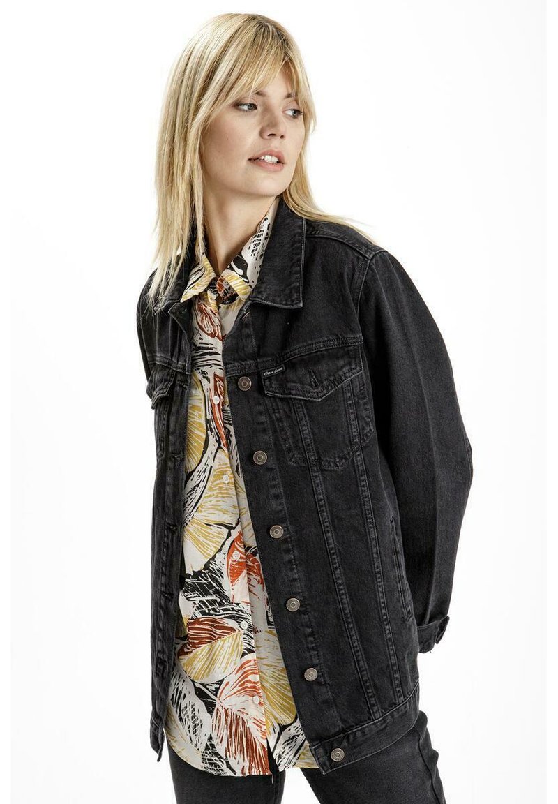 Czarna kurtka jeansowa z zapięciem na guziki i dwoma przednimi kieszeniami, nałożona na kolorową koszulę w wzory w odcieniach żółtego, czerwonego i czarnego.