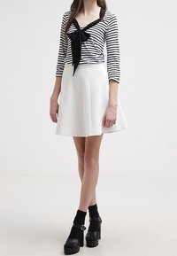 Randig svart och vit långärmad topp med en rosettdetalj, i kombination med en vit texturerad kjol. Svarta ankelboots med en kraftig klack.