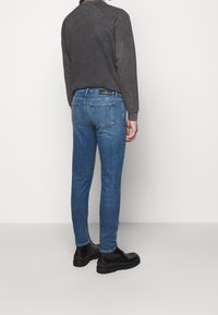 Smal blå denimjeans med fem fickor och en blekt baksida. Kombinerat med en mörkgrå crewneck-tröja och svarta stövlar.
