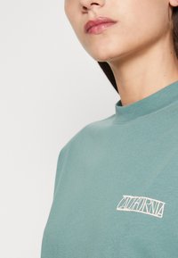 Teal cotton crewneck sweatshirt with a white "CALIFORNIA" graphic on the left chest. Smooth texture and relaxed fit.