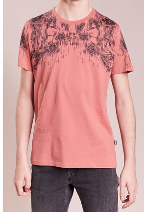 Kortærmet, koralfarvet T-shirt lavet af bomuld. Har et sort grafisk design med indviklede mønstre på den øverste front. Casual pasform.