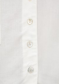 Chemise en lin blanc avec patte de boutonnage, ornée de boutons en coquillage iridescent et d'un tissu légèrement texturé. Douce et légère.