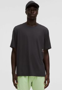 Tricou scurt, de culoare gri închis, dintr-un material moale, având un logo mic pe partea stângă și o gâtă rotundă. Asortat cu pantaloni scurți de culoare verde deschis.