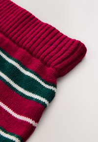 Puño de calcetín de punto acanalado rojo con patrones a rayas en verde, blanco y rojo. Textura suave que delimita la transición entre colores.