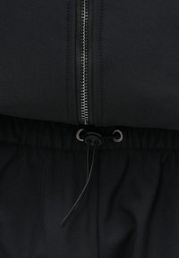 Μαύρο αθλητικό σακάκι με ασημένιο φερμουάρ και κορδόνι στη μέση. Το υλικό φαίνεται μαλακό με λεία υφή, σχεδιασμένο για άνεση και �ευελιξία.