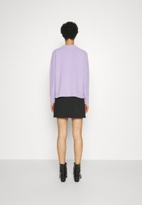 Lila trui met een relaxte pasvorm, ronde hals en ribbelzoom, gecombineerd met een zwarte mini-rok en zwarte enkelboots.