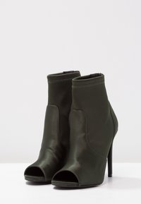 Gröna satängankelboots med öppen tå, hög stilettohæl, slät finish och elastiskt midja vid ankeln.