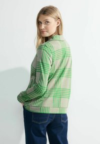 Suéter beige claro con diseño de cuadros verdes; presenta mangas largas, un cuello y un corte holgado. Material de punto texturizado.