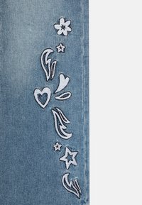 Tejido de mezclilla azul claro con diseños bordados en blanco, que incluyen flores, corazones y estrellas, dispuestos verticalmente por un lado.