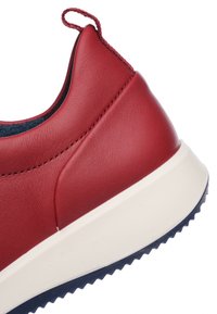 Red leather sneaker featuring a raised heel and contrasting white rubber sole with textured grip. The design includes a pull tab on the heel.