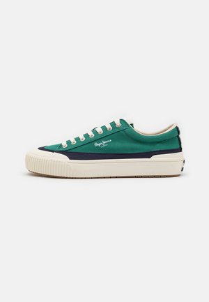 Zapatilla de lona verde y azul marino con una suela de goma blanca, puntera redonda y cordones crema que presentan un logo bordado en el lateral.