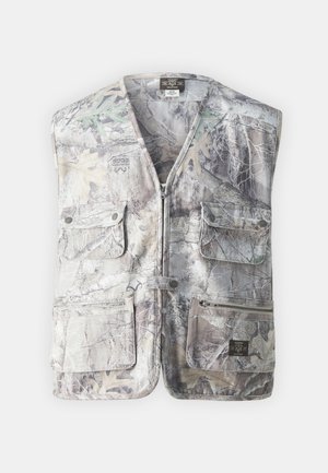 Kamovest med glidelås foran, flere lommer og en blanding av grå, beige og grønne mønstre som ligner på løvverk og barkteksturer.