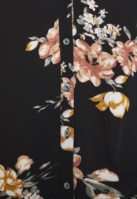 Schwarze Bluse mit floralem Muster, die rosa und gelbe Blumen zeigt, mit einer Knopfleiste vorne und einer glatten, leichten Stofftextur.