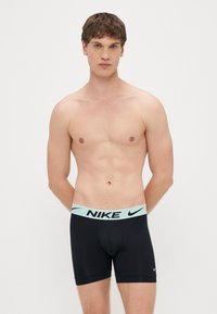 Mustad venivad bokserid helerohelise Nike logo vöökohaga, mis on keha lähedane ja ulatuvad keskreie kõrguseni. Sile tekstuur, ilma mustriteta.