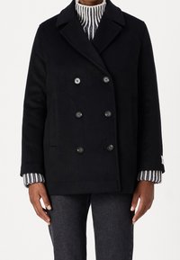 Zwarte wollen dubbelbreasted jas met grote knopen, zijzakken en een geknipt kraag, over een gestreepte trui. Zachte textuur en getailleerde pasvorm.