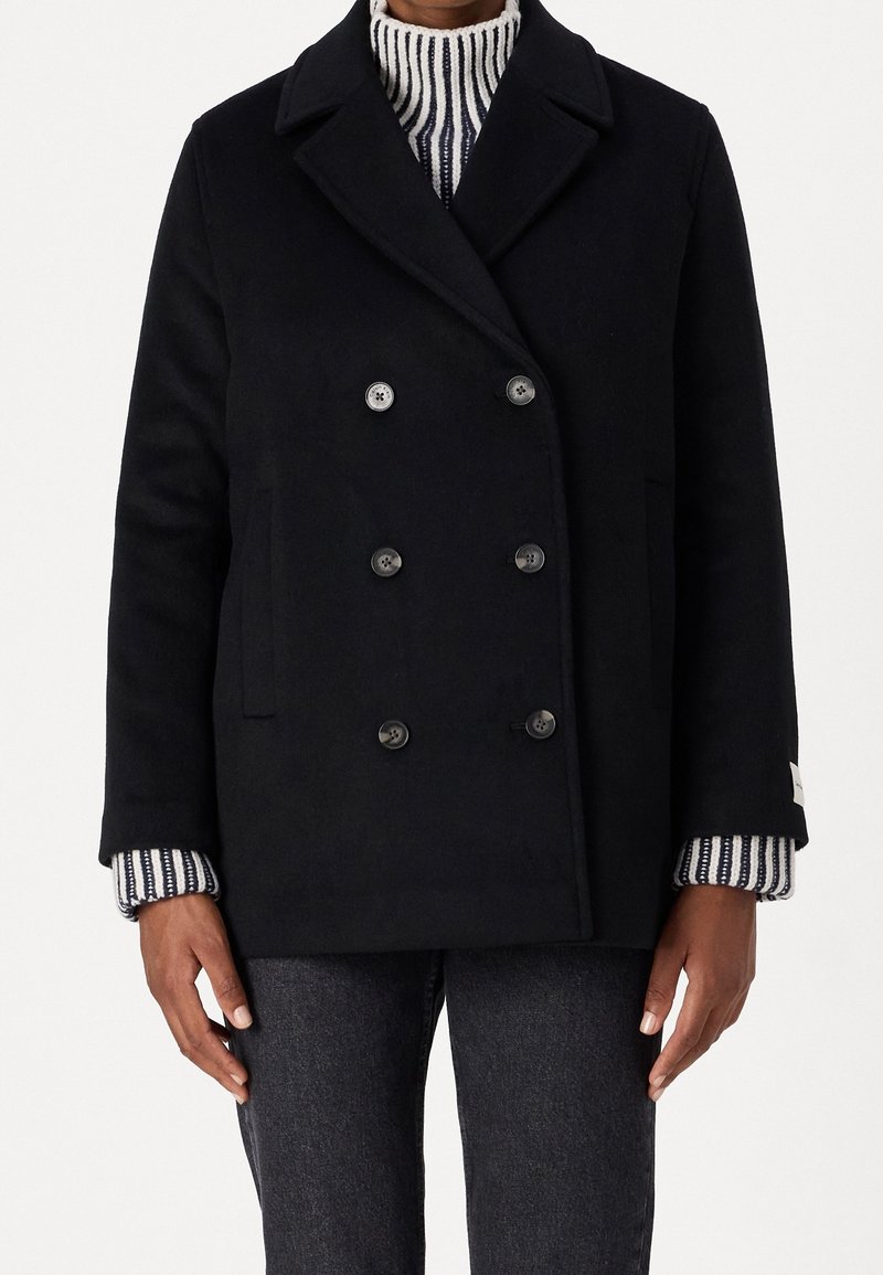 Zwarte wollen dubbelbreasted jas met grote knopen, zijzakken en een geknipt kraag, over een gestreepte trui. Zachte textuur en getailleerde pasvorm.