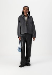 Veste courte en mélange de laine grise avec un col, fermeture à bouton et poches latérales, associée à un pantalon en cuir noir et un sac à main bleu clair.
