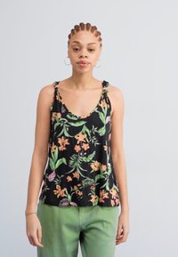 Débardeur noir à motifs floraux, ornés de fleurs orange et vert vif, avec des bretelles nouées, associé à un pantalon vert.