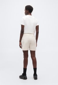 Άτομο που στέκεται με την πλάτη προς τα πίσω, φορώντας λευκό κοντομάνικο πουκάμισο, μπεζ σορτς, μαύρες κάλτσες και μαύρα παπούτσια για τρέξιμο σε μονοπάτια.