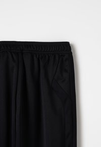 Schwarze Sporthosen mit glatter Textur, elastischem Bund und tailliertem Schnitt. Mit seitlichen Taschen und kontrastierenden Mesh-Details.