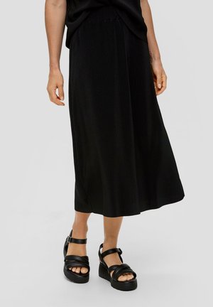 Zwarte geplooide midi-rok met een gladde textuur, gecombineerd met stevige zwarte platformsandalen met gekruiste bandjes en een gesp.