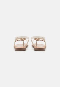 Sandali bianchi in pelle con strap sottili e una piccola fibbia, suola piatta marrone, che mostrano un design minimalista e una struttura aperta sulla punta.