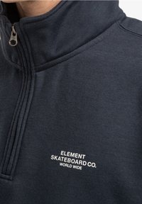Granatowy sweter z pół zamkiem wykonany z miękkiego materiału, z wysokim kołnierzem i białym haftem z logo "ELEMENT SKATEBOARD CO. WORLD WIDE".