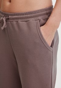 Bequeme Jogginghosen in einem gedeckten Mauve-Ton. Hergestellt aus weichem Stoff mit einem elastischen Bund, Kordelzug und Seitentaschen. Sanfte Textur.