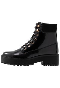Bottines en cuir verni noir avec une semelle épaisse, des ferrures dorées et des lacets ronds. Comprend un col en suede noir doux.