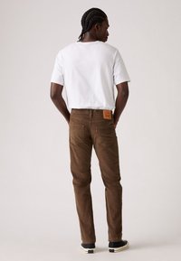 Pantaloni in corduroy marroni con tasche posteriori e una evidente etichetta in pelle sulla vita. Abbinati a una T-shirt bianca semplice.