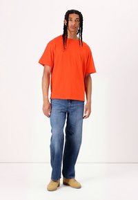 Oranje katoenen T-shirt met een losse pasvorm, korte mouwen, gecombineerd met blauwe rechte jeans en tan schoenen. Eenvoudig ontwerp, geen patronen.