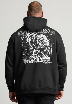 Hombre con sudadera negra con capucha con el logo de la banda Iron Maiden y gráfico "The Number of the Beast" en blanco en la espalda.