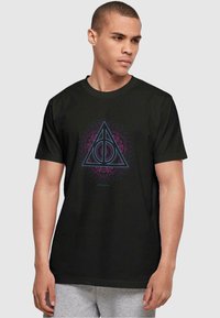 Camiseta de manga corta negra con un diseño geométrico triangular que presenta acentos en púrpura y azul, centrado en el pecho sobre un fondo sólido.