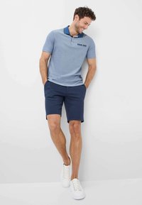 Polo azzurro chiaro con maniche corte, colletto blu navy e tasca sul petto. Abbinato a pantaloni corti blu scuro e sneakers bianche.
