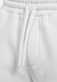 Bílé tepláky s šňůrkou v pase, boční kapsou, měkkou bavlněnou tkaninou a strukturovaným povrchem.