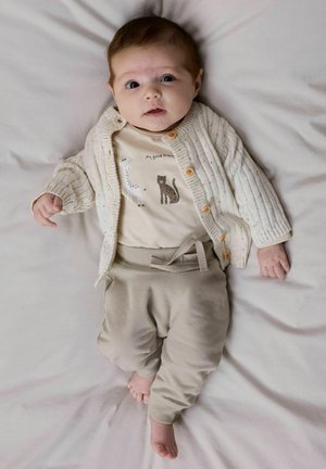Beige cardigan med ribbet tekstur og treknapper over en kremhvit body med dyreprint. Myke beige bukser med knytt belte.
