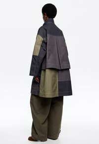 Overmaatse jacket met een mix van donkergrijze en olijfgroene stoffen; beschikt over een gestructureerd ontwerp, knoopaccenten en een lange achterkant.