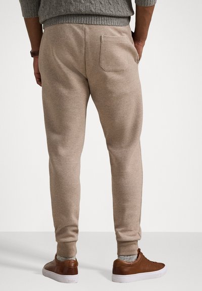 Beige sweatpants with elastic cuff and waistband, featuring a single back pocket; paired with brown sneakers and grey knitted sweater.