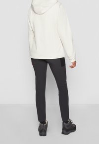 Veste blanche à capuche, pantalons ajustés noirs et chaussures foncées. Tissu lisse, coupe décontractée, poignets élastiques, détail de panneau subtil sur les pantalons.