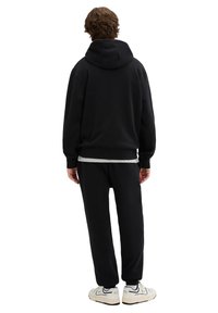 Sudadera con capucha negra y pantalones jogger a juego hechos de tela suave. Cuenta con un bolsillo tipo canguro y puños acanalados, combinados con zapatillas blancas.