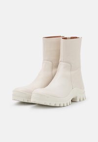 Botas de tobillo de cuero blancas con superficie texturizada y suelas de goma blanca gruesas, con un diseño elegante y detalles de costura mínimos.