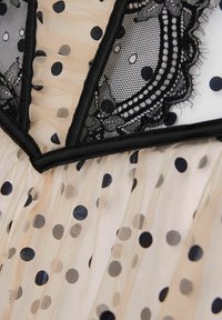 Černá síťovina s puntíky na nahém podkladu, zdobená krajkovým lemem a strukturovanou korzetovou částí s kontrastním lemováním. Měkká, průsvitná textura po celém povrchu.